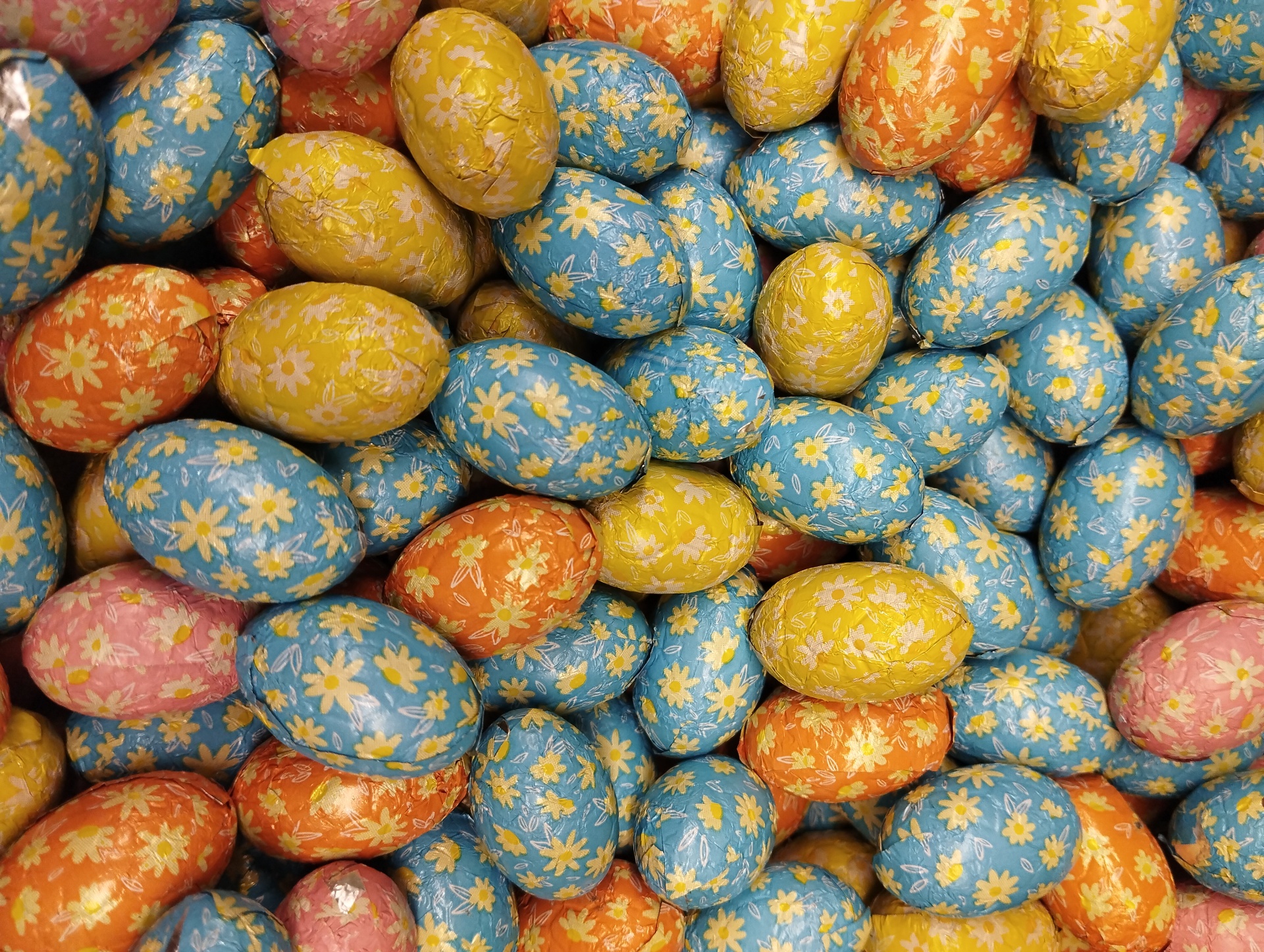 Ovos decorativos coloridos com padrão de flores amarelas sobre fundo azul, amarelo, laranja e rosa