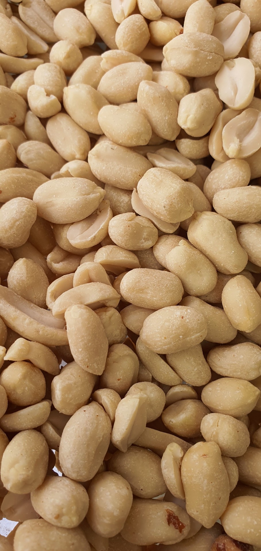 Amendoins descascados bege claro com textura lisa, texto parcial 'NUS' e 'FARINHA' visível.