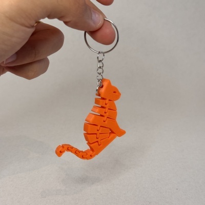 Porta-chaves com pendente de dinossauro laranja a ser segurado por uma mão.