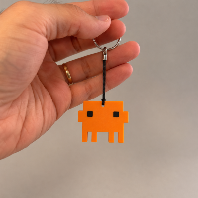 Chaveiro personagem pixelada laranja com olhos pretos na mão