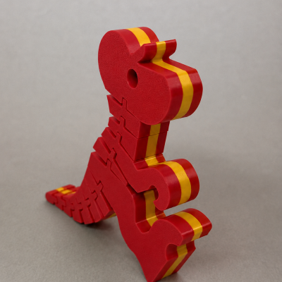 Objeto dinossauro vermelho de plástico com faixa amarela e laranja sobre fundo cinzento.