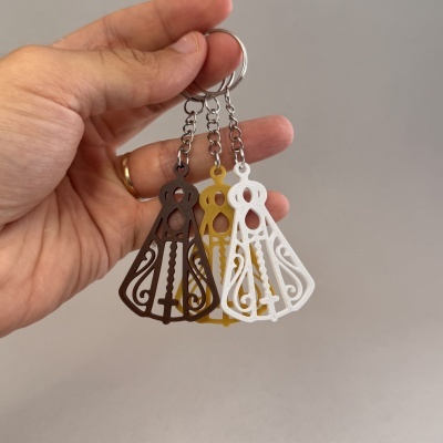 Chaveiros de metal com pingentes recortados em castanho, amarelo e branco segurados por mão com anel dourado