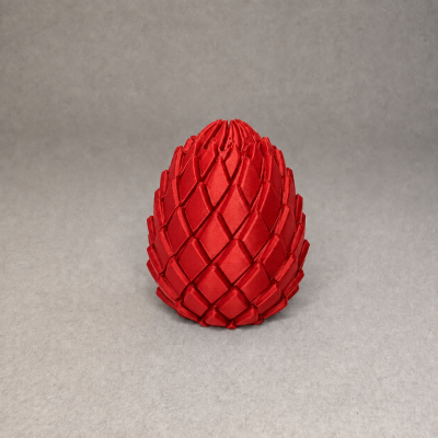 Objeto decorativo vermelho em forma de piña com textura em escamas, sobre superfície cinza.