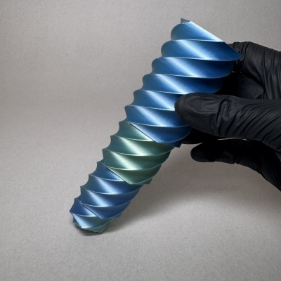 Peça metálica azul helicoidal segurada com luva preta