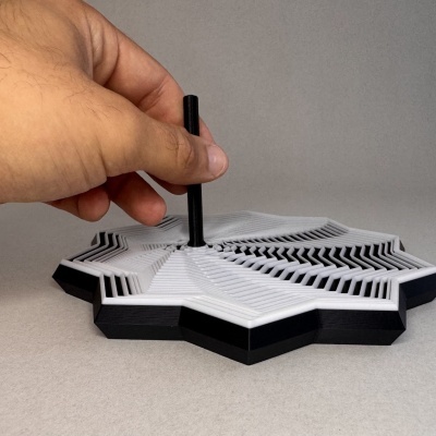 Objeto 3D hexagonal preto e branco com camadas, segurado por mão humana.