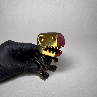 Figura de dinossauro dourado e vermelho segurada por mão com luva preta
