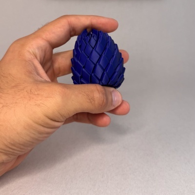 Mão segurando objeto azul com textura de escamas em fundo cinza