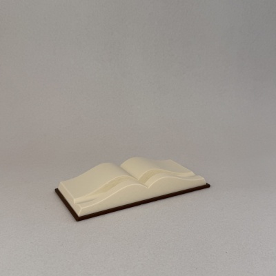 Escultura decorativa de livro aberto em tom creme numa base castanha sobre fundo cinzento