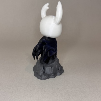 Estatueta de personagem com capa preta sobre base de pedras cinzenta