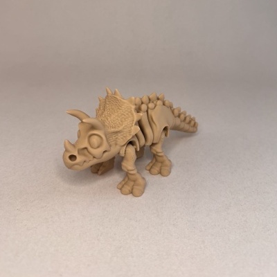 Figura Triceratops bege com textura lisa e detalhes de ossos num fundo neutro.