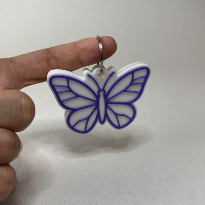 Chaveiro borboleta branco e roxo segurado entre dedos