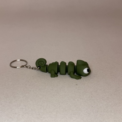 Chaveiro camaleão verde em superfície bege