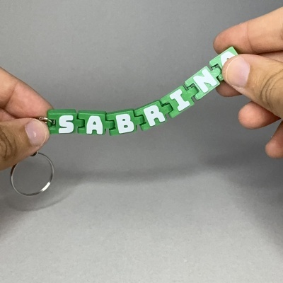 Chaveiro de plástico verde com letras brancas formando SABRINA