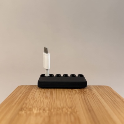 Cabo USB tipo C branco num suporte preto sobre mesa de madeira