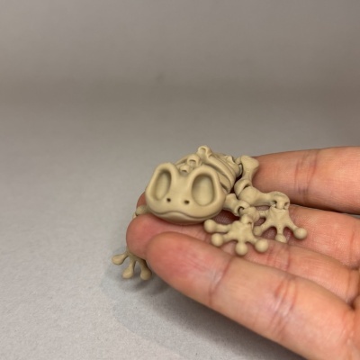 Miniatura de sapo bege em mão sobre fundo cinza