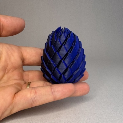 Objeto azul em forma de pinha decorativa com padrão de escamas, segurado pela mão