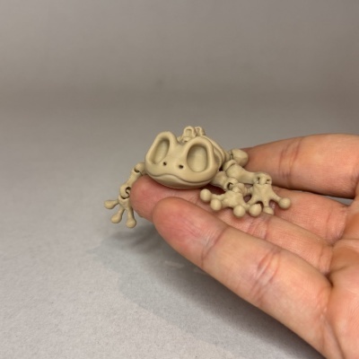 Boneco castanho claro pequeno em forma de sapo segurado por uma mão