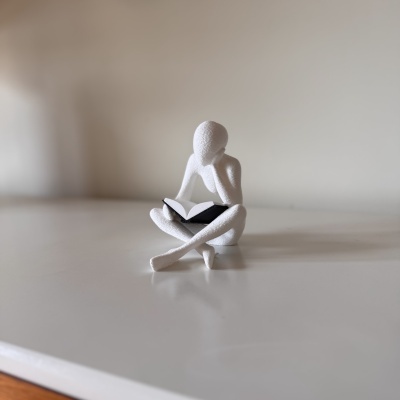 Figura decorativa branca sentada com livro aberto
