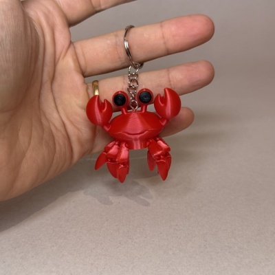 Chaveiro caranguejo vermelho em plástico brilhante, segurado por mão com anel dourado