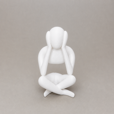 Estátua branca de figura humana sentada com mãos nas orelhas e pernas cruzadas