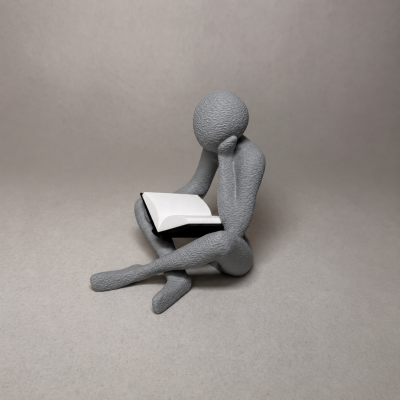 Escultura cinzenta de pessoa a ler um livro aberto com capa preta