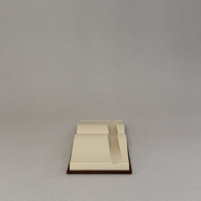 Miniatura arquitetónica creme sobre base castanha com fundo cinzento.