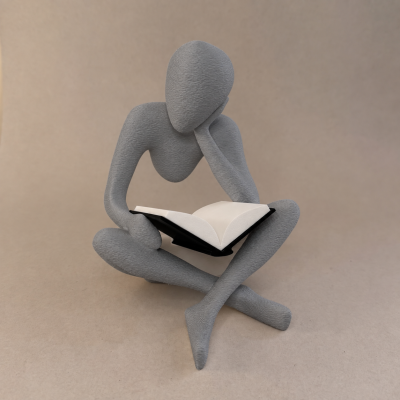 Escultura cinzenta de figura humana sentada lendo livro de capa preta