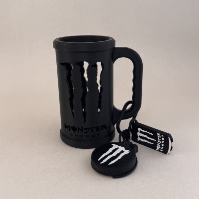 Copo preto Monster Energy com chaveiros ao lado em fundo cinzento