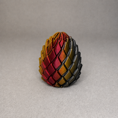 Escultura em forma de ovo com padrão escamado em vermelho, amarelo e preto