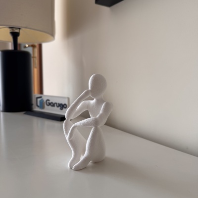 Escultura abstrata branca de figura humana a pensar numa superfície branca
