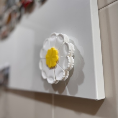 Objeto branco em forma de flor com centro amarelo numa superfície branca com parede de azulejos bege