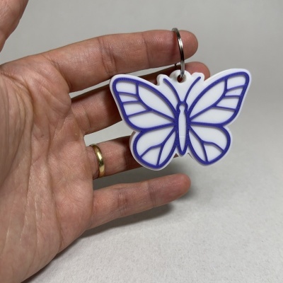 Chaveiro plástico branco e roxo em forma de borboleta na mão
