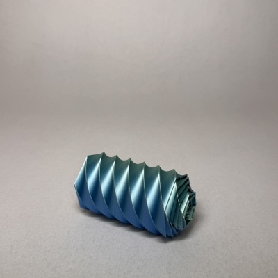 Objeto azul metálico com textura ondulada em superfície cinza claro