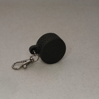 Chaveiro redondo preto com presilha metálica prateada em fundo cinzento.