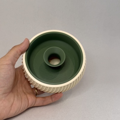 Objeto circular verde e bege com textura canelada na parte externa segurado por uma mão