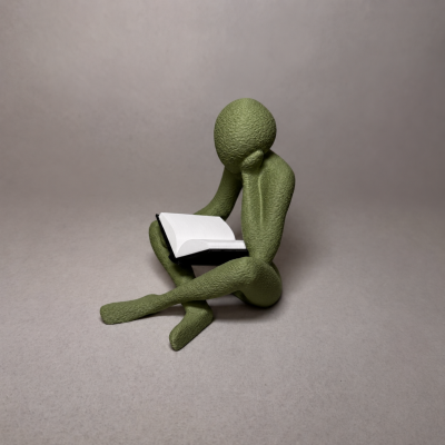 Estatueta verde de figura humana sentada a ler um livro sobre fundo cinzento