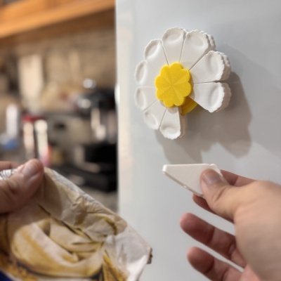 Marca-roupa magnético em forma de flor com pétalas brancas e centro amarelo numa superfície branca