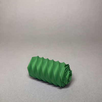 Objeto cilíndrico verde com padrão espiral em relevo sobre superfície cinza