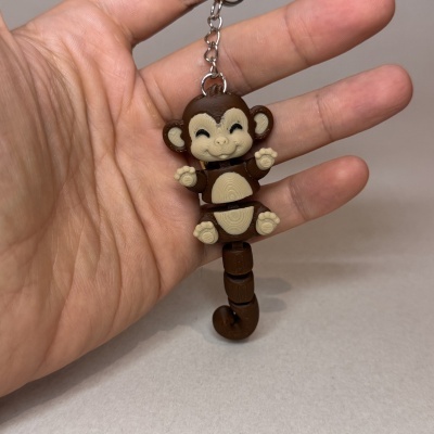 Chaveiro de macaco sorridente castanho e bege com cauda articulada numa mão.
