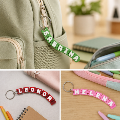 Porta-chaves personalizados em blocos verdes, vermelhos e rosa com nomes, em mochilas e superfícies diversas.