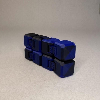 Fidget cube azul e preto com texturas e padrões geométricos sobre superfície cinzenta