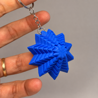 Porta-chaves azul em forma de estrela tridimensional a ser segurado por uma mão.