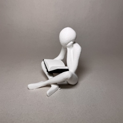 Escultura branca de figura humana sentada a ler um livro aberto