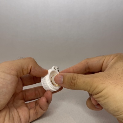Dispositivo circular branco com textura e parte central dourada segurado por mãos