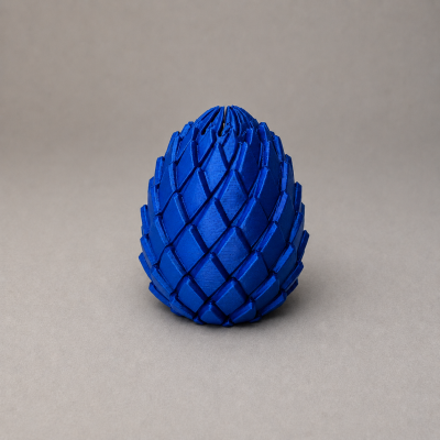 Objeto decorativo azul em forma de cone com textura de escamas sobre uma superfície cinza.