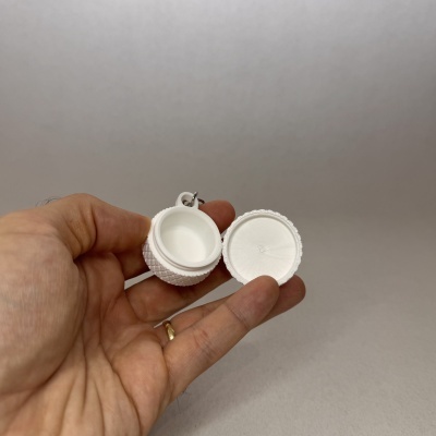Recipiente pequeno branco com tampa destacável segurado por mãos em fundo cinzento.