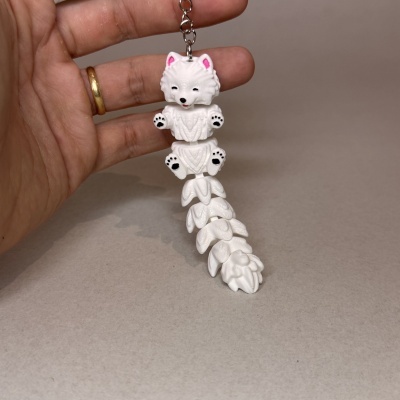 Chaveiro pendente de cães brancos empilhados com detalhes em rosa e preto, segurado por mão com anel dourado