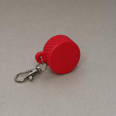 Chaveiro vermelho cilíndrico em silicone com mosquetão prateado sobre superfície cinza clara
