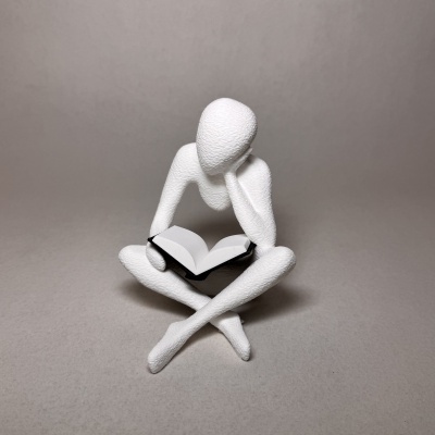 Estátua branca de figura humana sentada lendo livro