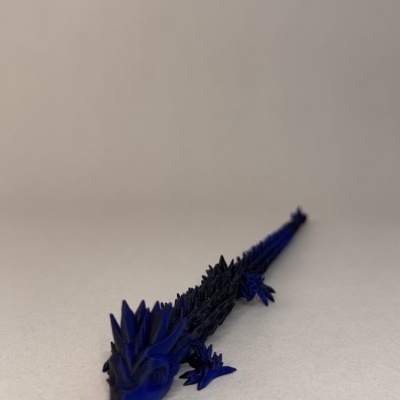 Figura decorativa azul escura e preta em forma de lagarto ou dragão sobre fundo cinza claro